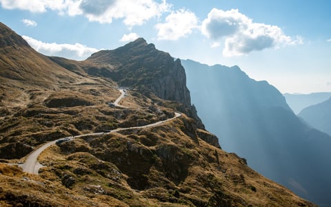 Cars driving on a winding mountain road through stunning alpine scenery under bright blue sky