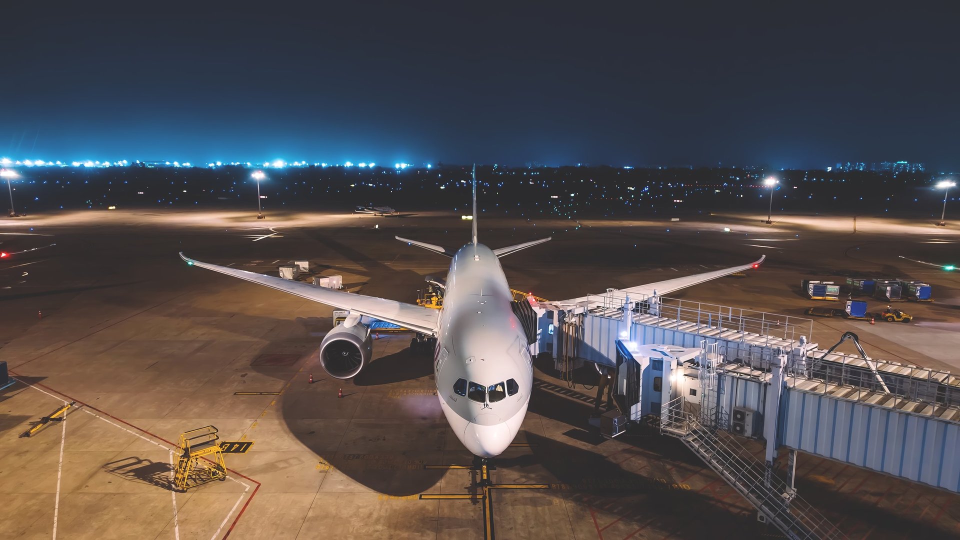 Commercial passenger airplane parked at an airport gate at night beside an illuminated runway, representing an international arrival