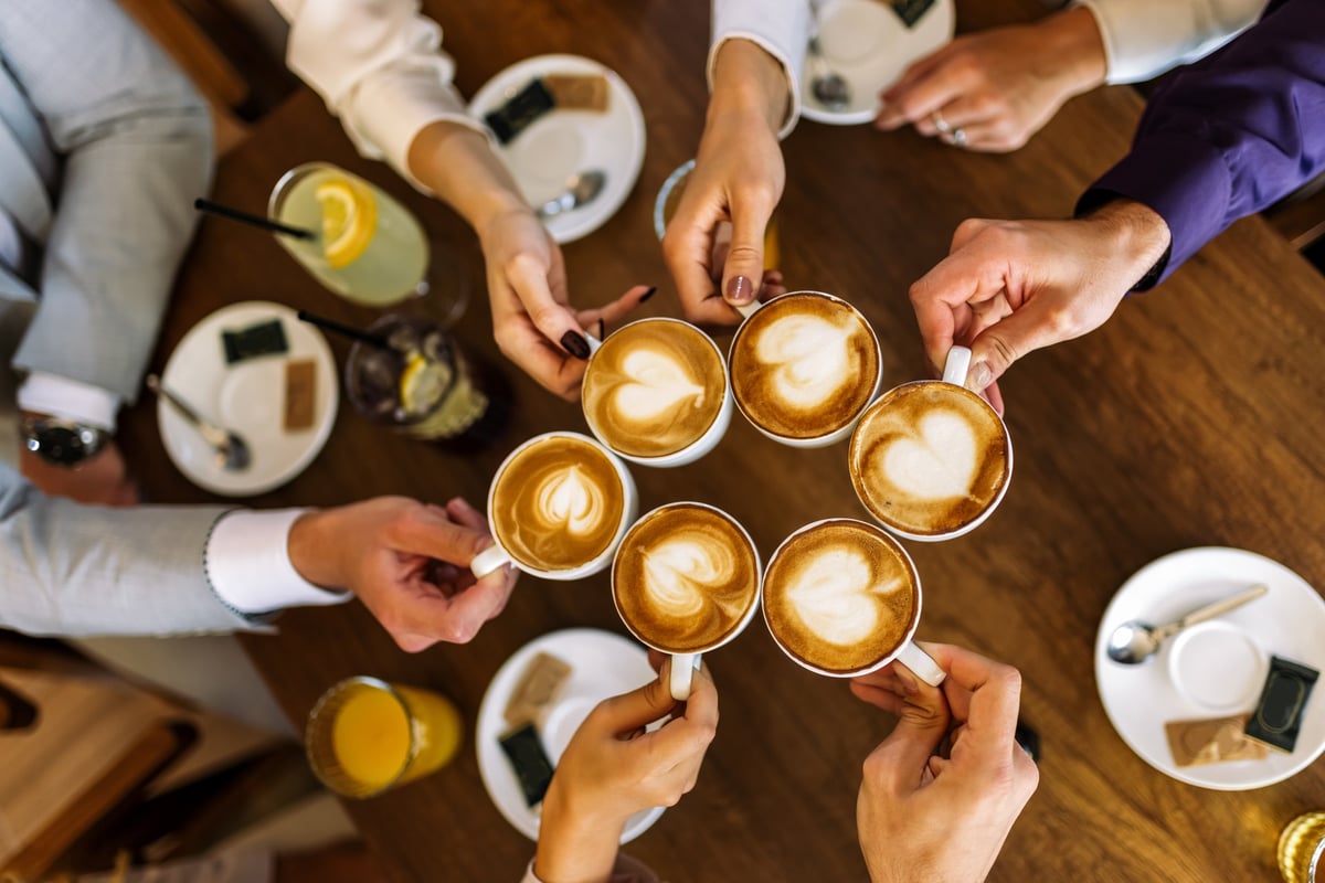 Close-up of friends clinking coffee cups together at a café table