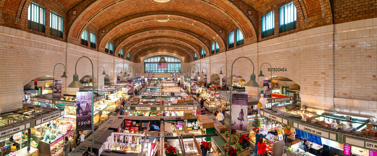 Wide angle view of a busy covered market hall with shoppers walking through the corridors beneath a historic roof structure