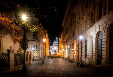 A charming night scene of a cobblestone street in Bucharest, Romania, with illuminated historic buildings and a distant cathedral