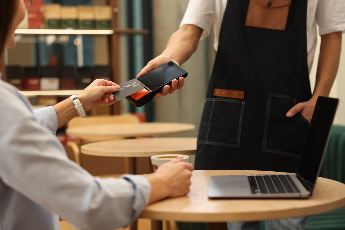 Woman paying with a card at a wooden cafe table