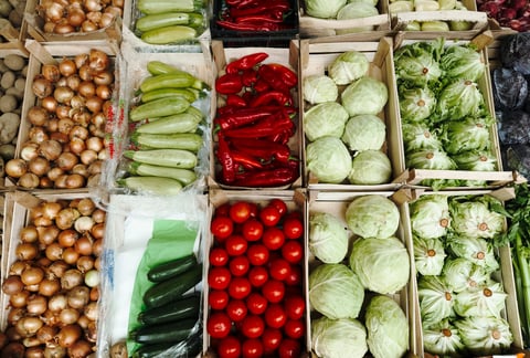 Overhead view of assorted vegetables neatly arranged in wooden crates at a local market, showing fresh onions, peppers, cabbage, zucchini and tomatoes