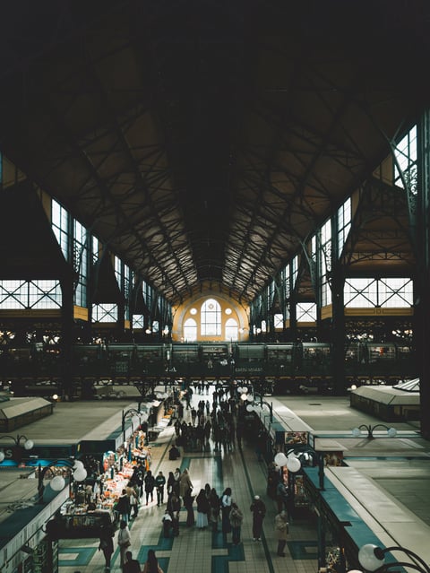 Visitors walking through a historic covered market hall in Budapest, Hungary, surrounded by food stalls beneath a large iron and glass roof