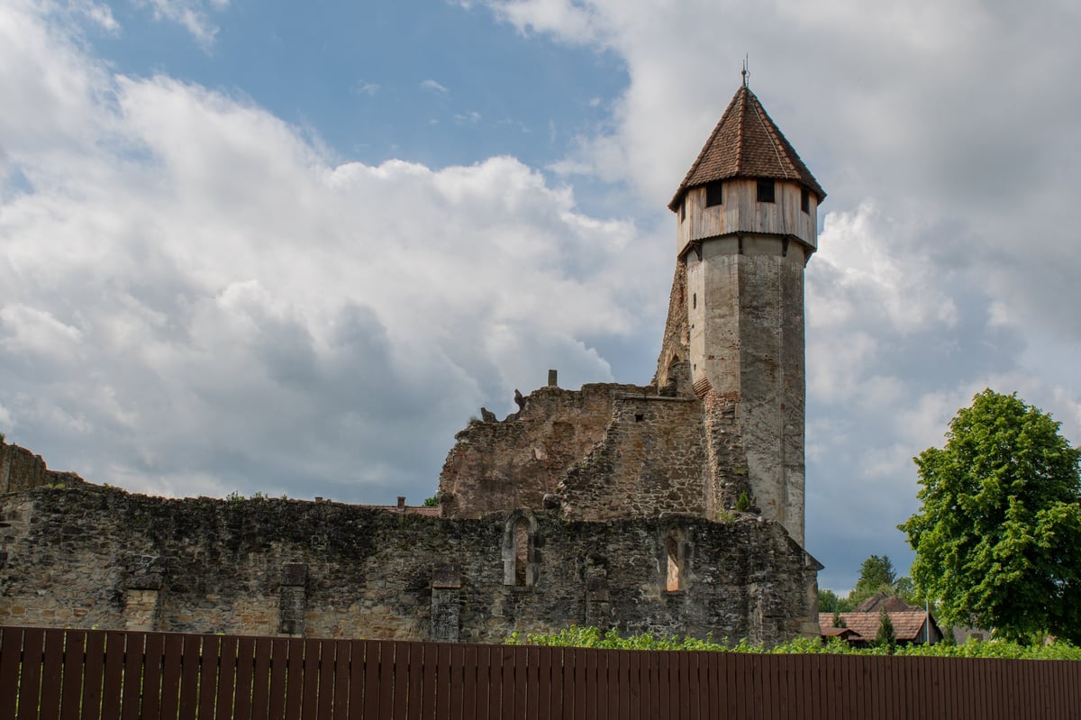 Stone fortress ruins with a tall church tower under a cloudy spring sky in rural Transylvania
