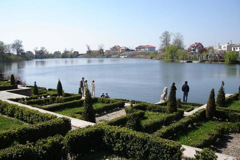 Formal garden with manicured hedges overlooking a calm lake and residential houses across the water on a clear day