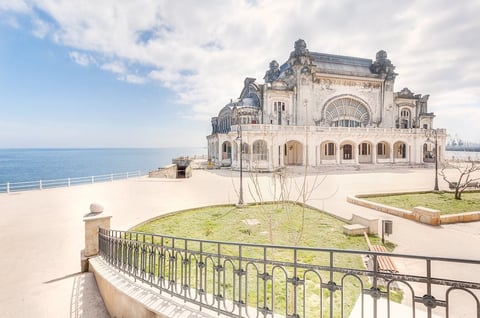 Ornate white beachfront building with domed turrets overlooking the sea, surrounded by a metal railing and manicured grounds