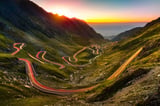 Winding mountain road with long exposure car light trails at sunset in green valley landscape