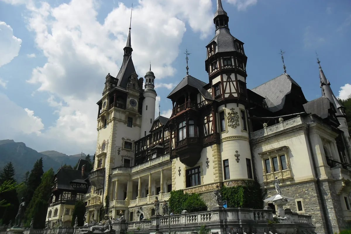 Peleș Castle exterior with its white and timbered towers set against a blue sky within woody foothills of the Bucegi Mountains in Sinaia, Romania