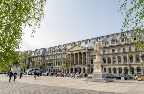 Grand European plaza with classical architecture, ornate buildings, statue monument, and people walking in a sunny public square