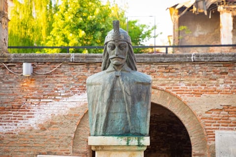 Stone bust sculpture mounted on pedestal in front of aged red brick wall with archway