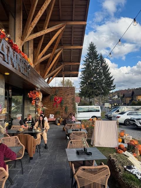 Outdoor patio seating area decorated with autumn foliage under wooden beam structure with diners enjoying refreshments