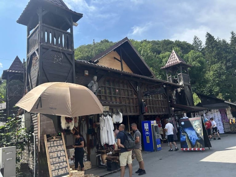 Medieval-style wooden building with towers at an outdoor market, visitors browsing stalls under umbrellas and blue canopies