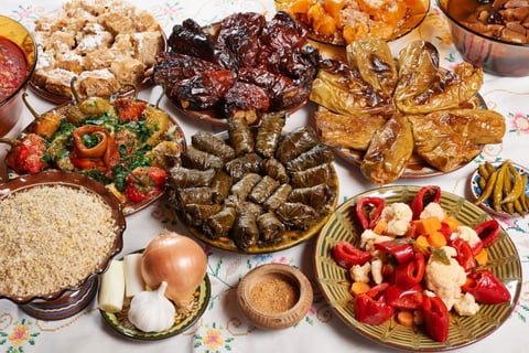 Overhead view of a diverse spread of prepared dishes including rice, roasted vegetables, red peppers, onions, herbs, and various cooked meats and appetizers on white background