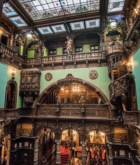 Ornate multi-level interior courtyard with green walls, carved wooden balconies, arched doorways, and glass skylight ceiling illuminated by warm lighting