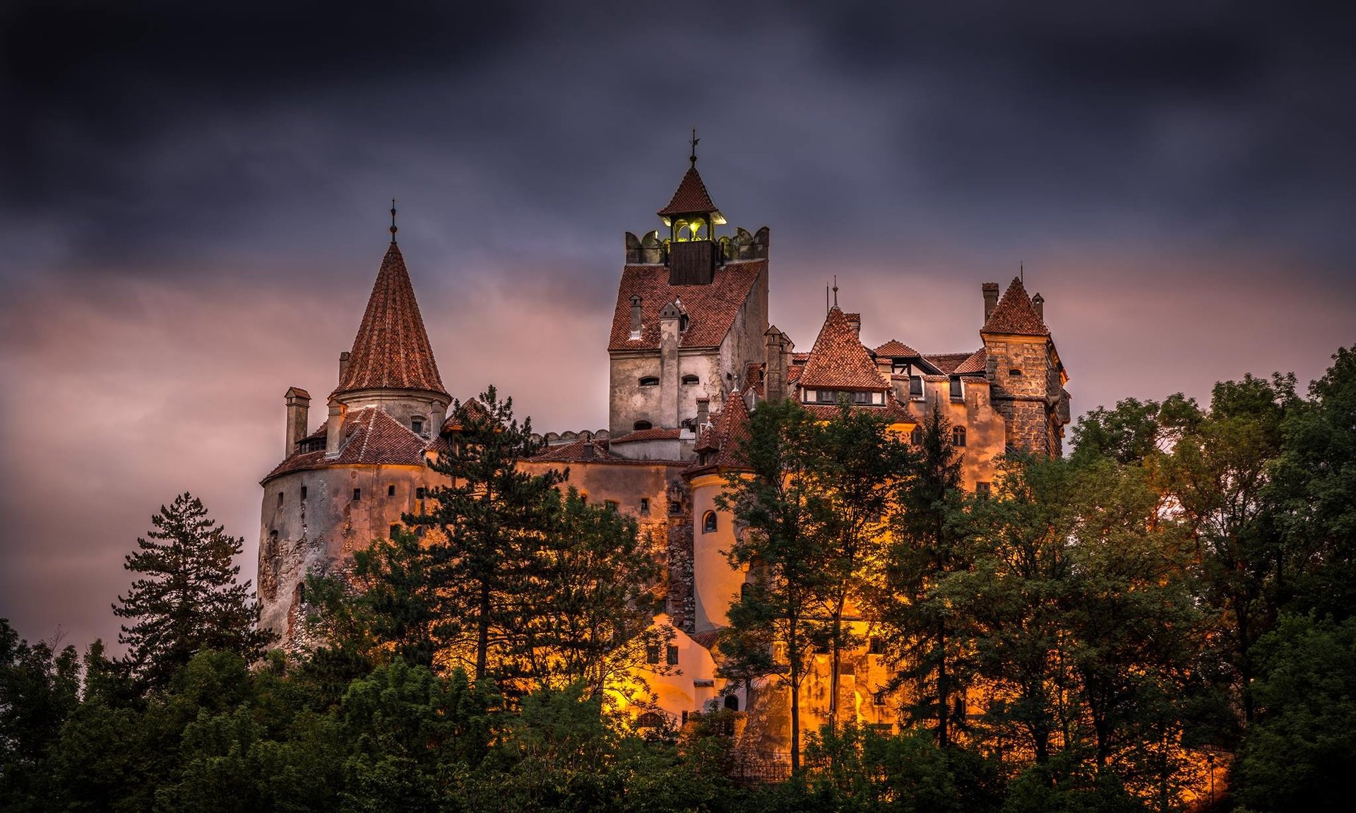 Bran Castle with its towers and red-tiled roofs rising on a rocky outcrop in the Carpathian foothills of Transylvania, surrounded by forest