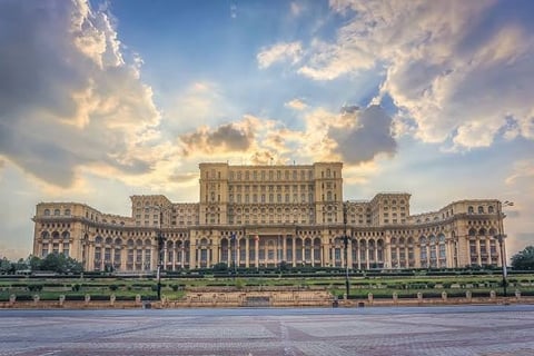 Large imposing government building with classical architecture reflected in waterfront plaza under dramatic cloudy sky