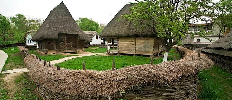 Two traditional thatched-roof houses with whitewashed walls in a historical open-air museum setting, surrounded by rustic wooden fence