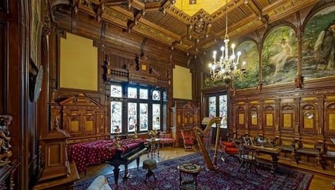 Ornate Victorian parlor with grand piano, wooden paneling, crystal chandelier, and decorative murals