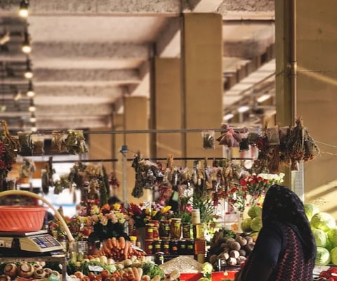 Indoor garden market or plant shop with hanging dried herbs and flowers, potted plants, and produce displayed on tables under natural light from windows