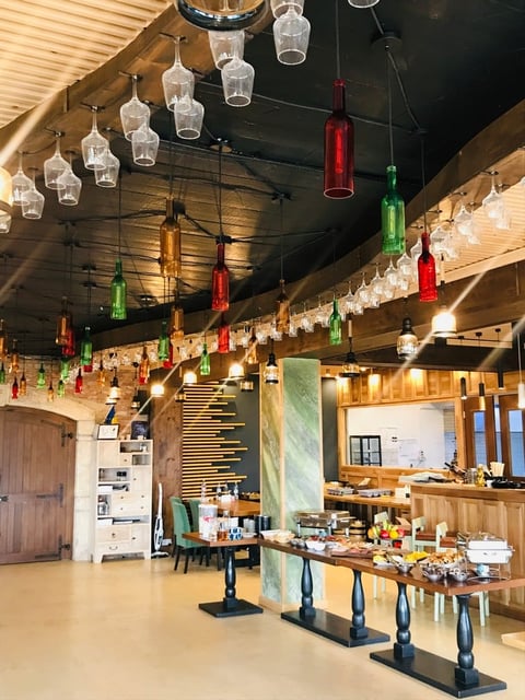 Modern restaurant interior with hanging colored glass bottle lights, wooden beams, and a service counter with bar seating