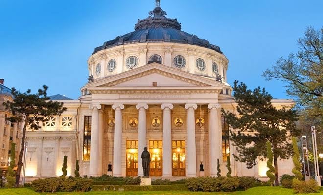 Romanian Athenaeum in Bucharest, a neoclassical concert hall with a domed roof and columns lit at dusk among the trees
