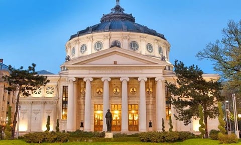 Neoclassical building with white columns and a large domed roof illuminated at dusk, surrounded by landscaping and trees