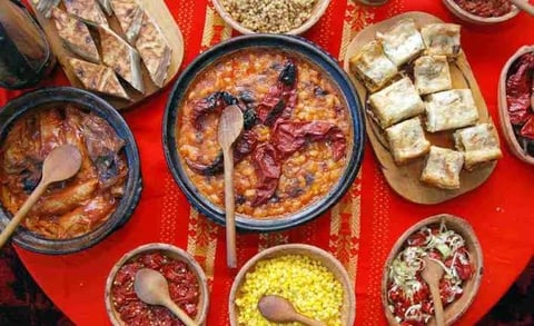Overhead view of Asian dishes and condiments on red surface, including soup bowls, tofu, nuts, and various sauces in small bowls