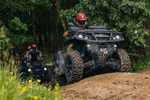 ATV rider in red helmet on dark four-wheeler on dirt trail with forest background and other riders visible in distance