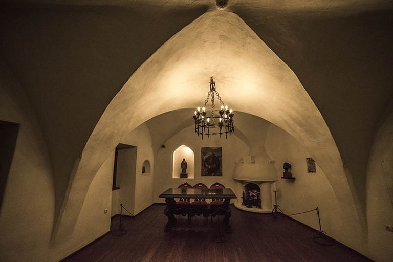 Interior of a vaulted stone chapel with a chandelier, altar, religious icons on walls, and arched ceiling