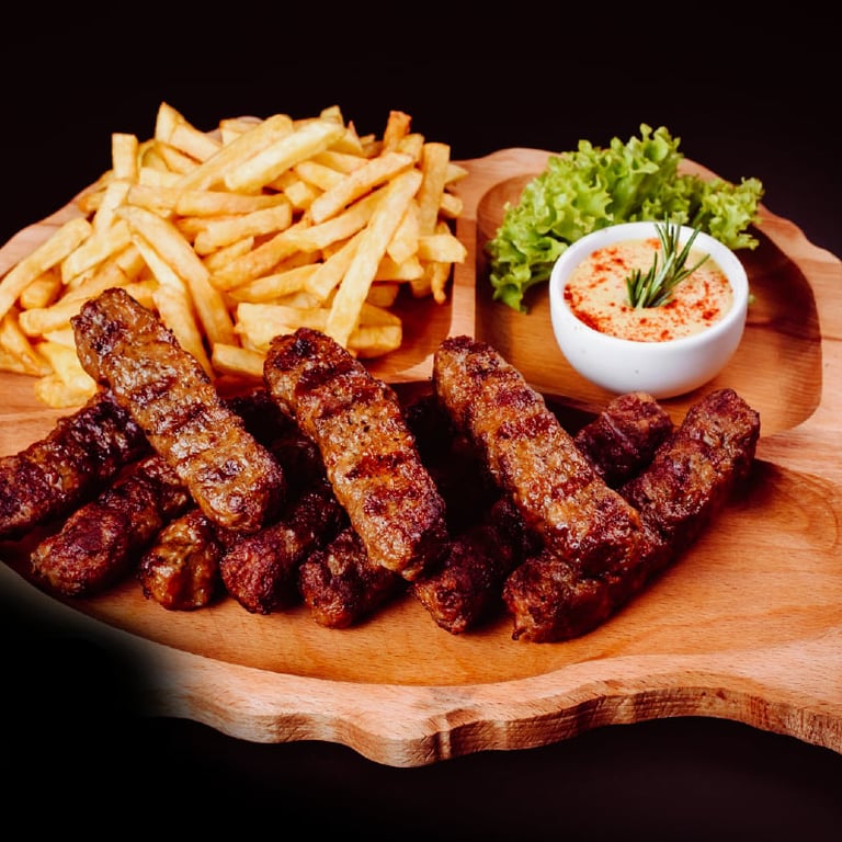 Grilled meat skewers with fries, hummus dip, and lettuce served on a wooden board