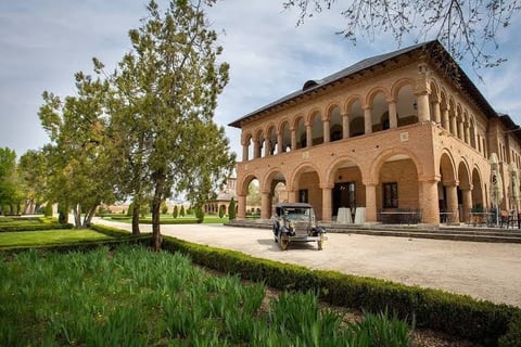 Historic brick Renaissance villa with arched windows and colonnade portico surrounded by trees and manicured grounds